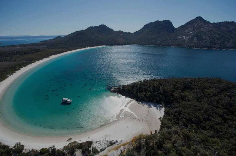 Sweeping view of Freycinet National Park, Tasmania, featuring the pink granite peaks of the Hazards, turquoise waters of Wineglass Bay, and lush coastal forest.