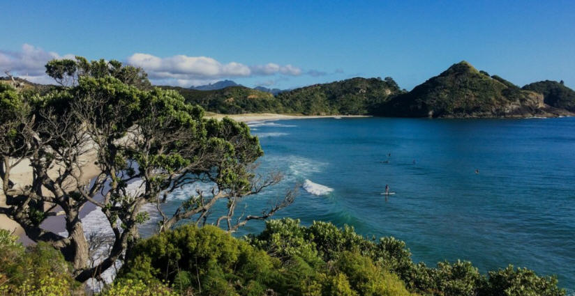 Sweeping view of Great Barrier Island, New Zealand, with rugged coastline, sandy beaches, and lush green hills.