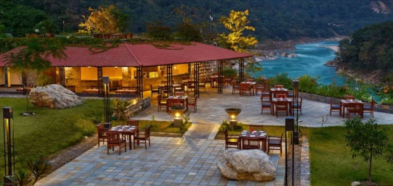 Rishikesh, India, where the sacred Ganges River emerges from the Himalayas, framed by lush green hills and suspension bridges.