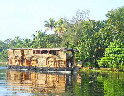 Lush green palm trees lining the tranquil backwaters of Kerala, India, with a traditional houseboat cruising along.