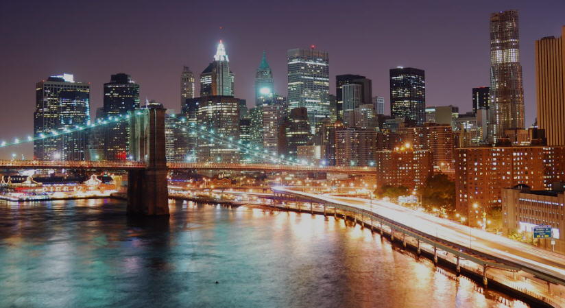 Panoramic view of New York City at dusk, showcasing a sea of skyscrapers illuminated against a vibrant sunset.