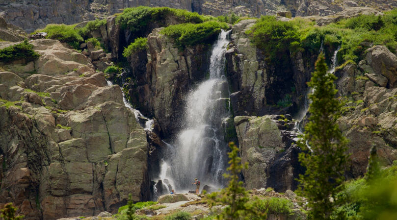 Chasm Lake nestled below towering cliffs in Rocky Mountain National Park, with wildflowers blooming in the foreground.