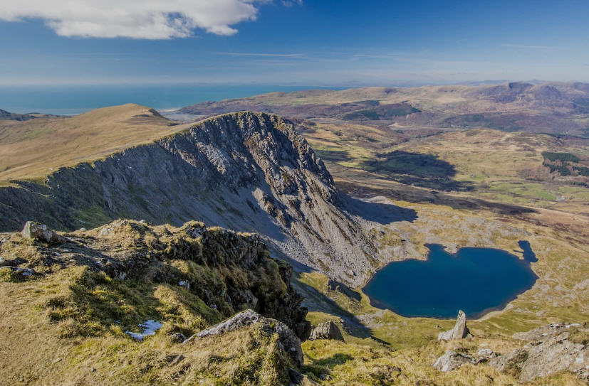 Panoramic vista of Snowdonia National Park at sunset, with dramatic clouds and fiery colors painting the sky.