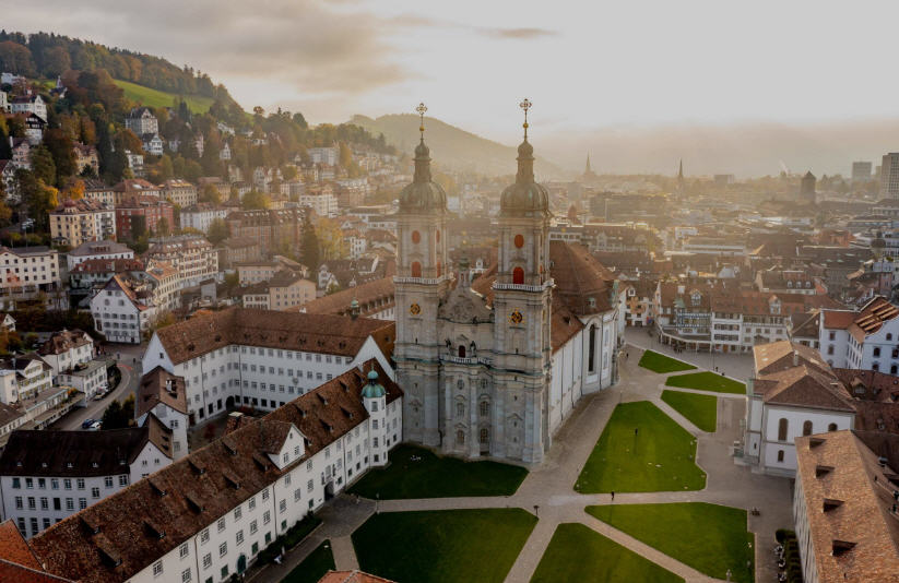 Panoramic view of St. Gallen, Switzerland, featuring the Baroque Abbey Cathedral, colorful Altstadt (Old Town), and rolling green hills.