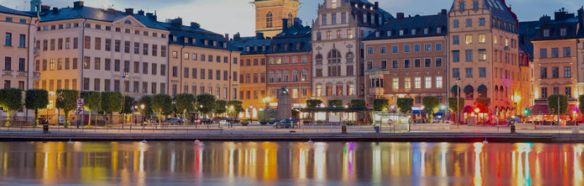 Stockholm skyline with colorful buildings of Gamla Stan (Old Town), City Hall's tower, and boats on the waterfront.