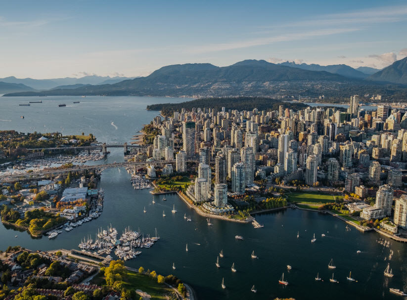Vancouver skyline featuring modern skyscrapers, the North Shore Mountains, and sailboats in Coal Harbour.