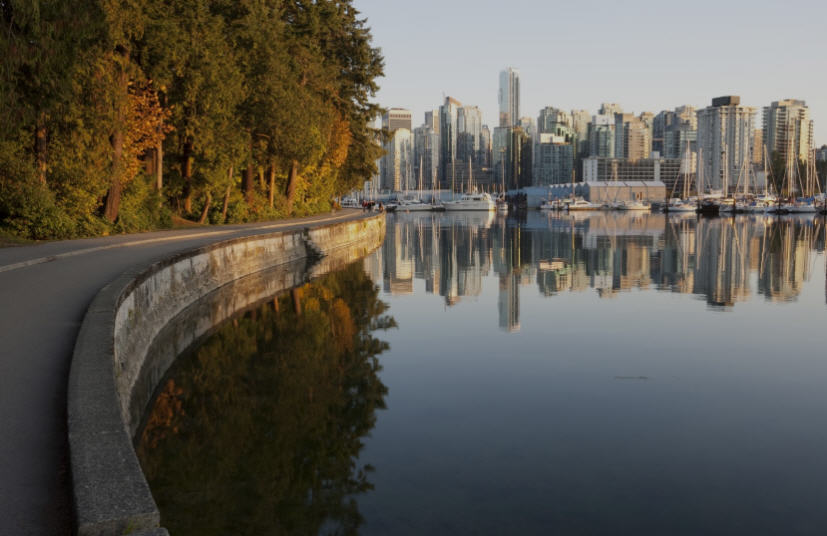 Seawall in Stanley Park, Vancouver, with cyclists, joggers, and views of the city skyline and harbor.
