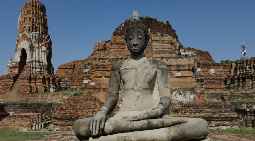 A lone monk in orange robes walking among the ruins of Ayutthaya, Thailand.