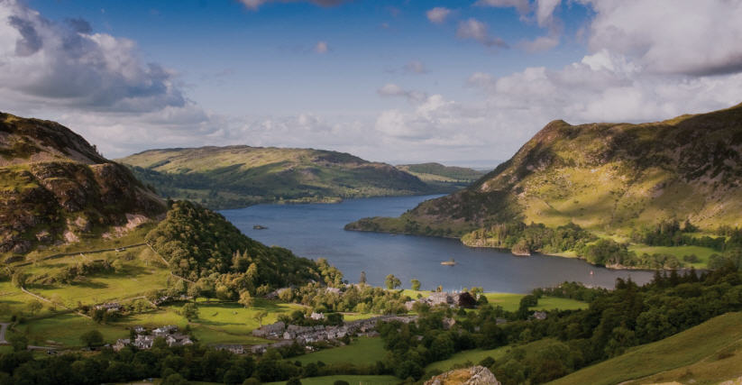 Rolling hills and a sparkling lake in the Lake District National Park, England, with quaint villages nestled in the distance.