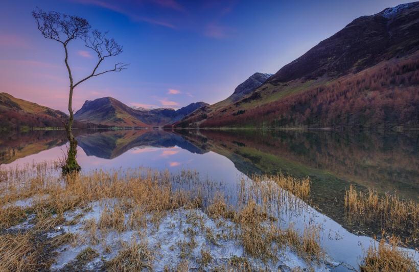 Dramatic Lake District landscape with rugged mountains, a winding stone wall, and grazing sheep under a stormy sky.
