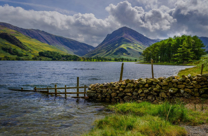 Family picnicking on the grassy shore of a Lake District lake, with children splashing in the shallows.